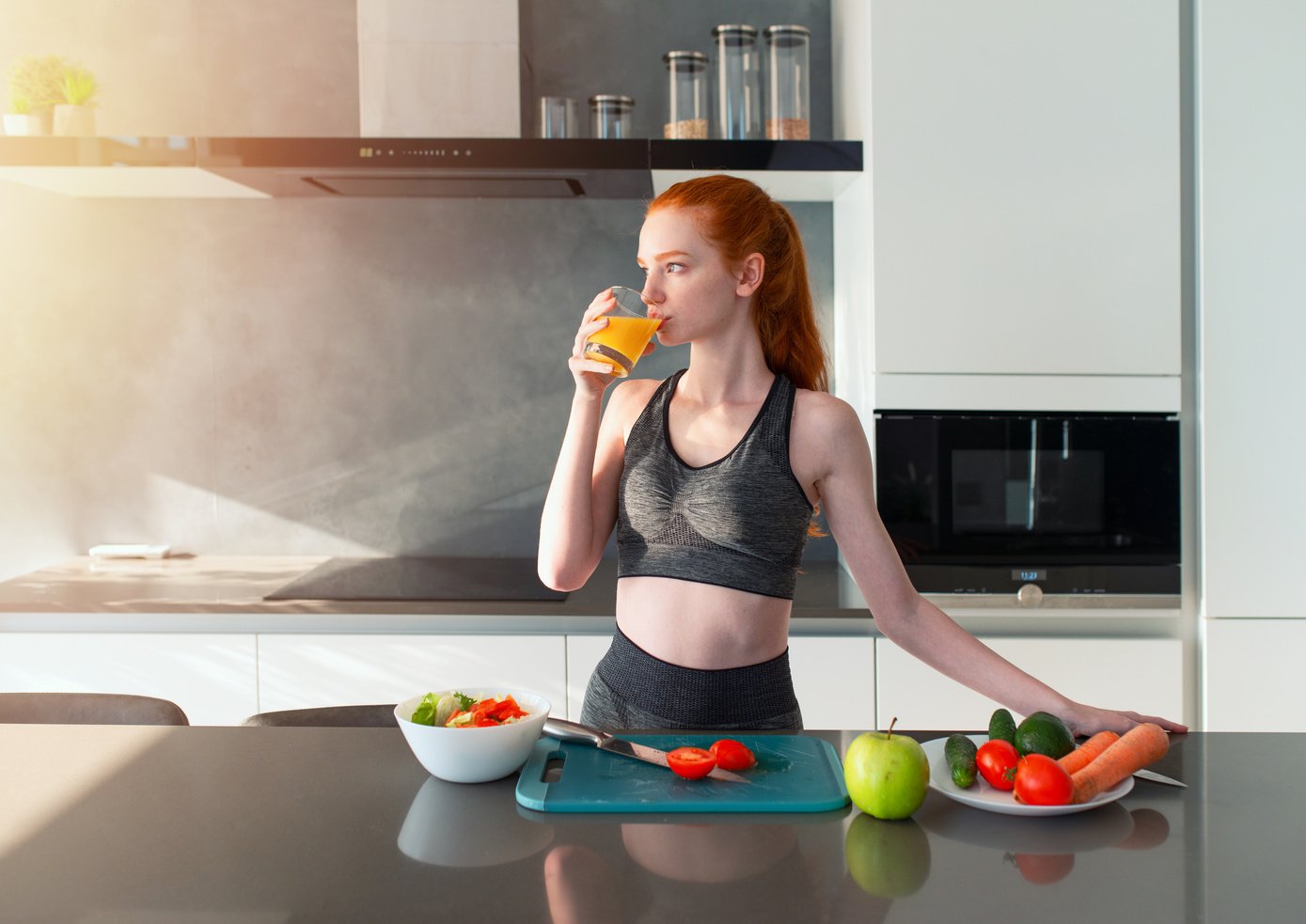 Athletic Girl with Gym Clothes Eats Fruit in the Kitchen