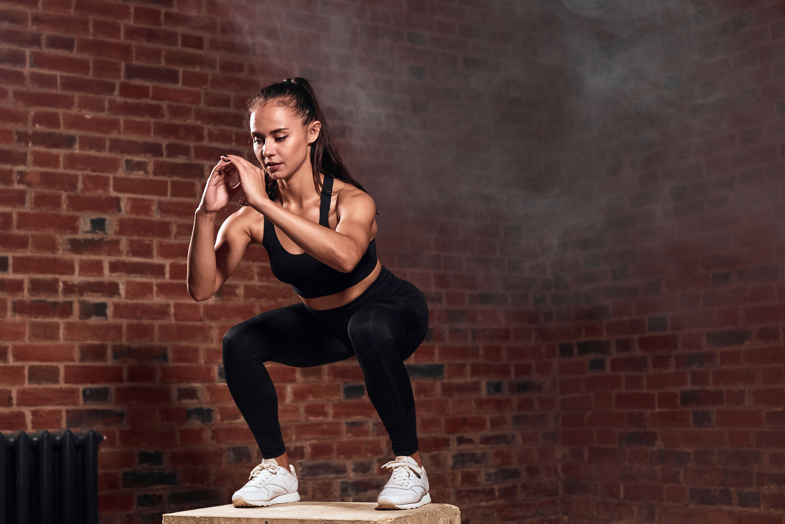 Beautiful female bodybuilder performing squats jumping on fit box in gym